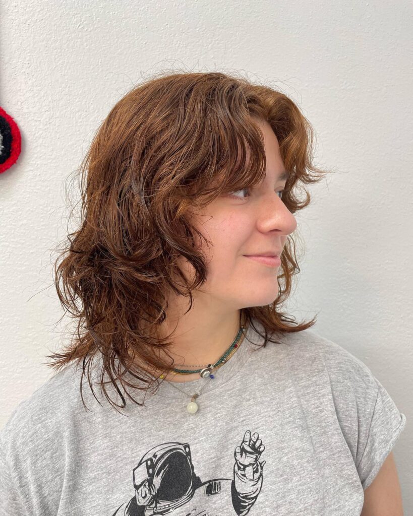A layered curly lob with auburn tones and soft curtain bangs.