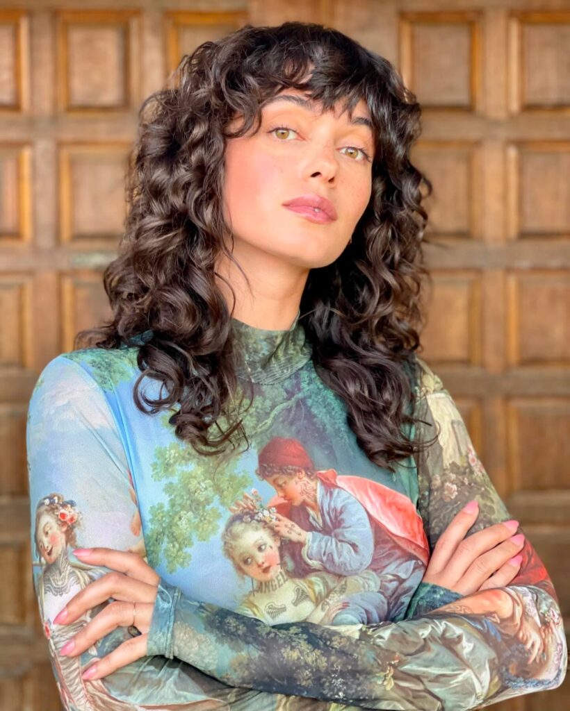 A voluminous curly lob with tight dark curls and a short micro fringe.