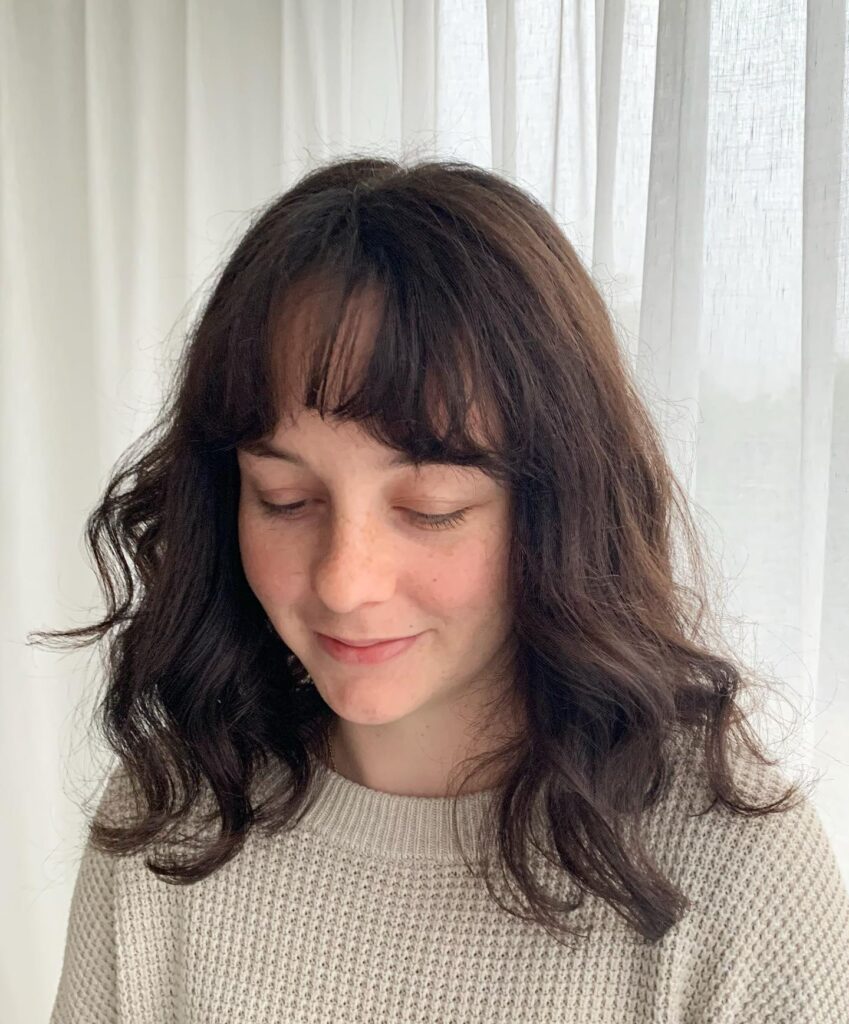 A soft wavy lob with dark brown hair and light wispy bangs.