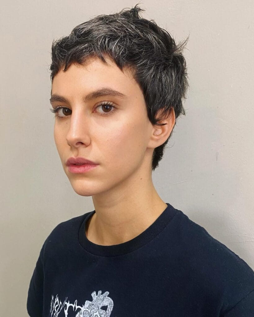 Short textured pixie haircut with soft micro bangs and natural dark hair.