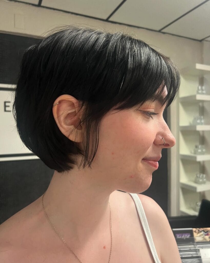 Short rounded tomboy bob with soft bangs and a tapered nape in dark hair.
