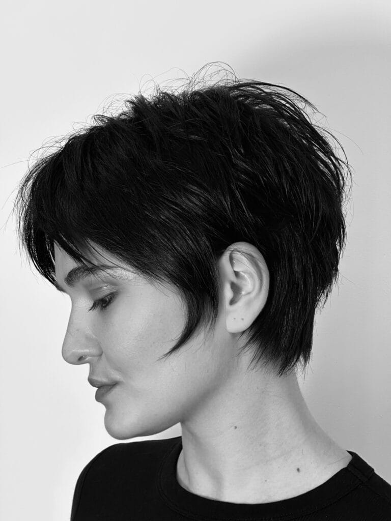 Short layered tomboy pixie haircut with choppy texture and a soft side fringe in dark hair.