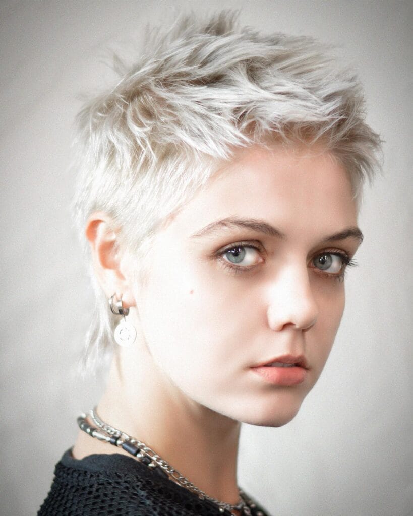 Short icy blonde tomboy pixie haircut with textured layers and a slightly spiky top.