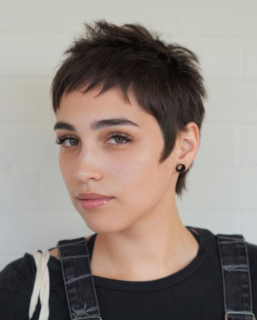 Short tousled tomboy pixie haircut with wispy fringe and soft textured layers in brunette hair.