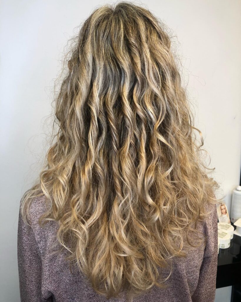Long blonde curly hair with soft textured waves and natural highlights viewed from the back.