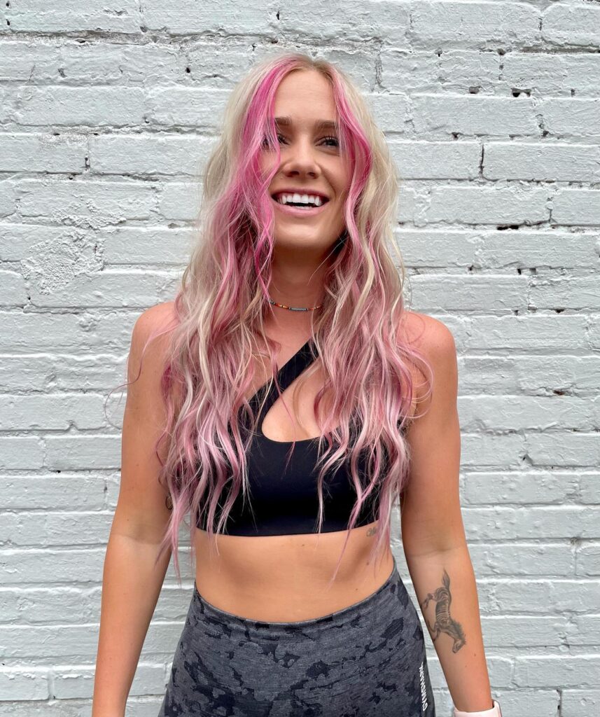 Long wavy blonde hair with pink streaks and soft layered texture.