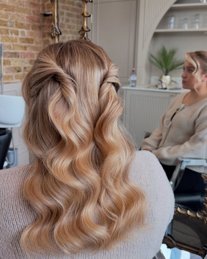 Long blonde wavy hair styled in a soft twisted half up half down hairstyle with smooth flowing waves.