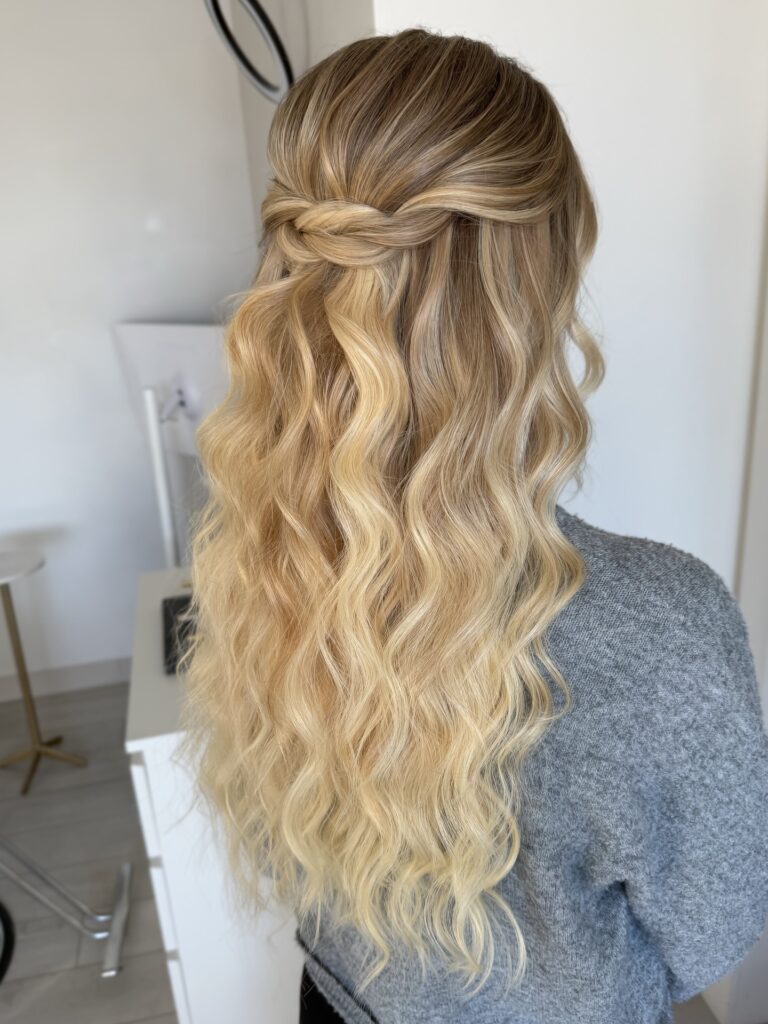 Long blonde wavy hair styled in a loose braided half up half down hairstyle with soft texture.