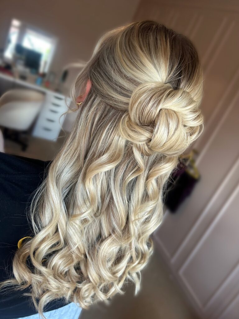Long blonde curly hair styled in a twisted knot half up half down hairstyle with soft curls.