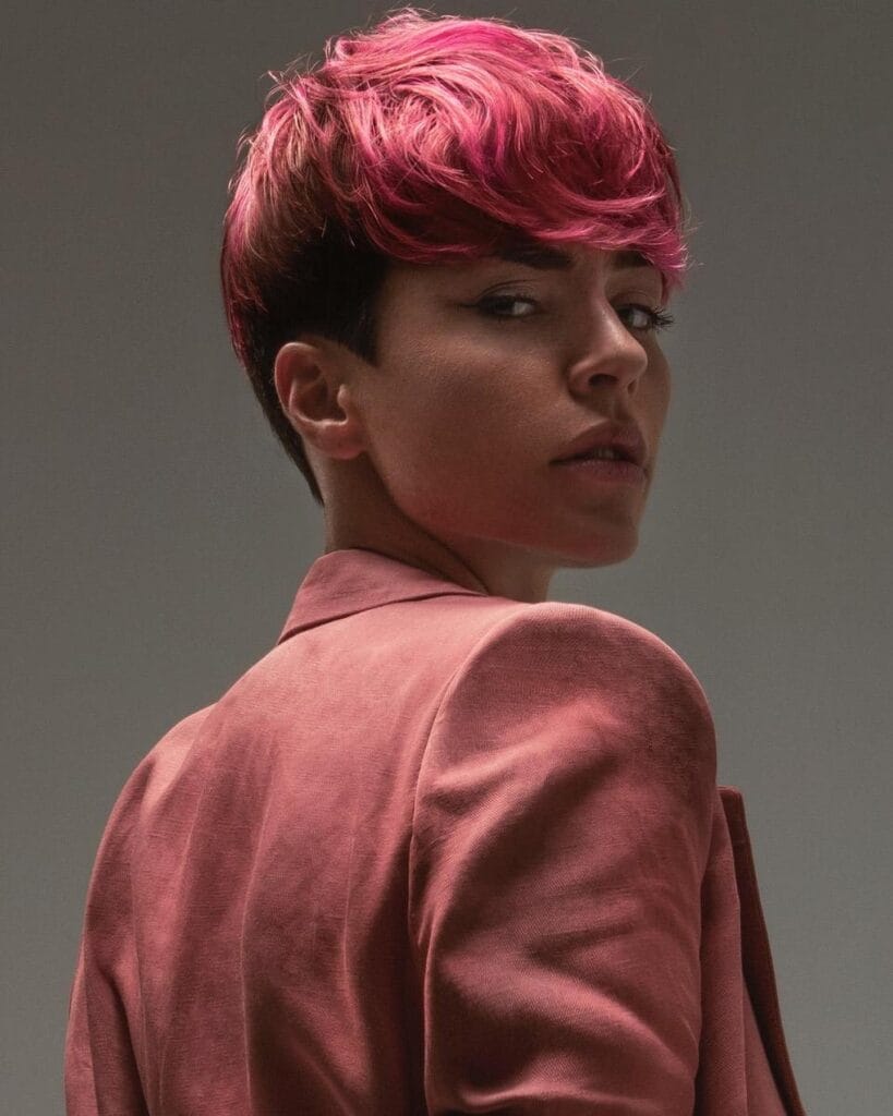 A woman with a short pixie haircut featuring a textured long top and vibrant pink hair color.