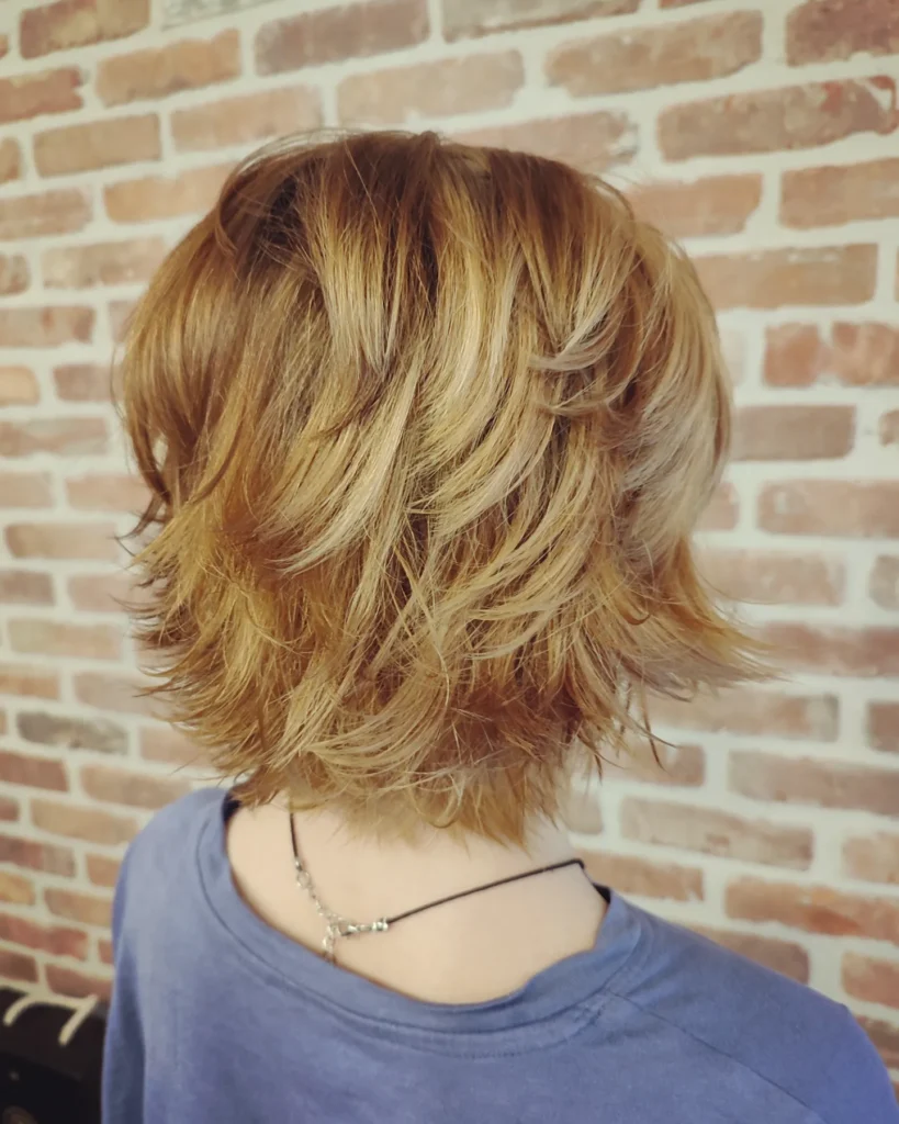 Short shaggy tomboy bob haircut with soft layers and warm blonde tones with textured ends.