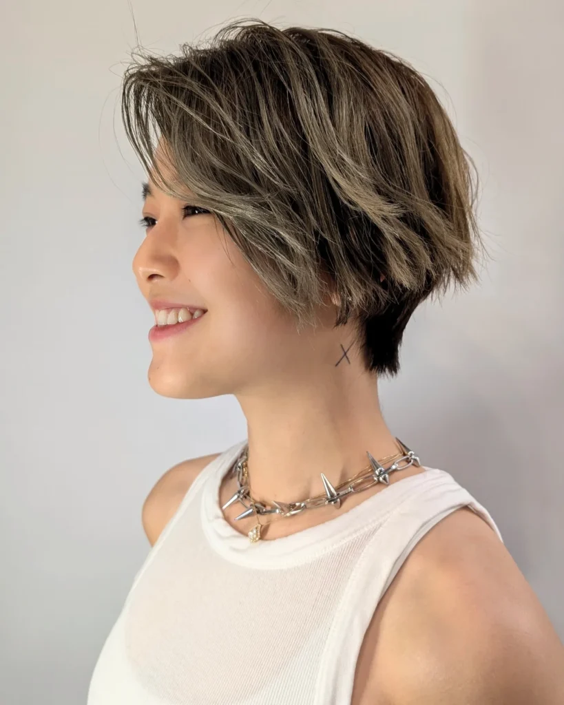 Short layered tomboy bob with a tapered nape and soft ash brown highlights.