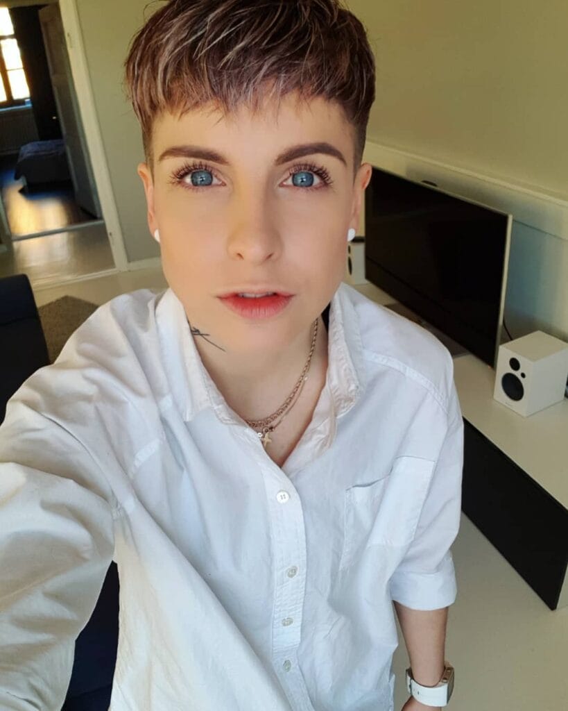 Very short tomboy pixie haircut with soft textured top and cropped sides in warm brown hair.