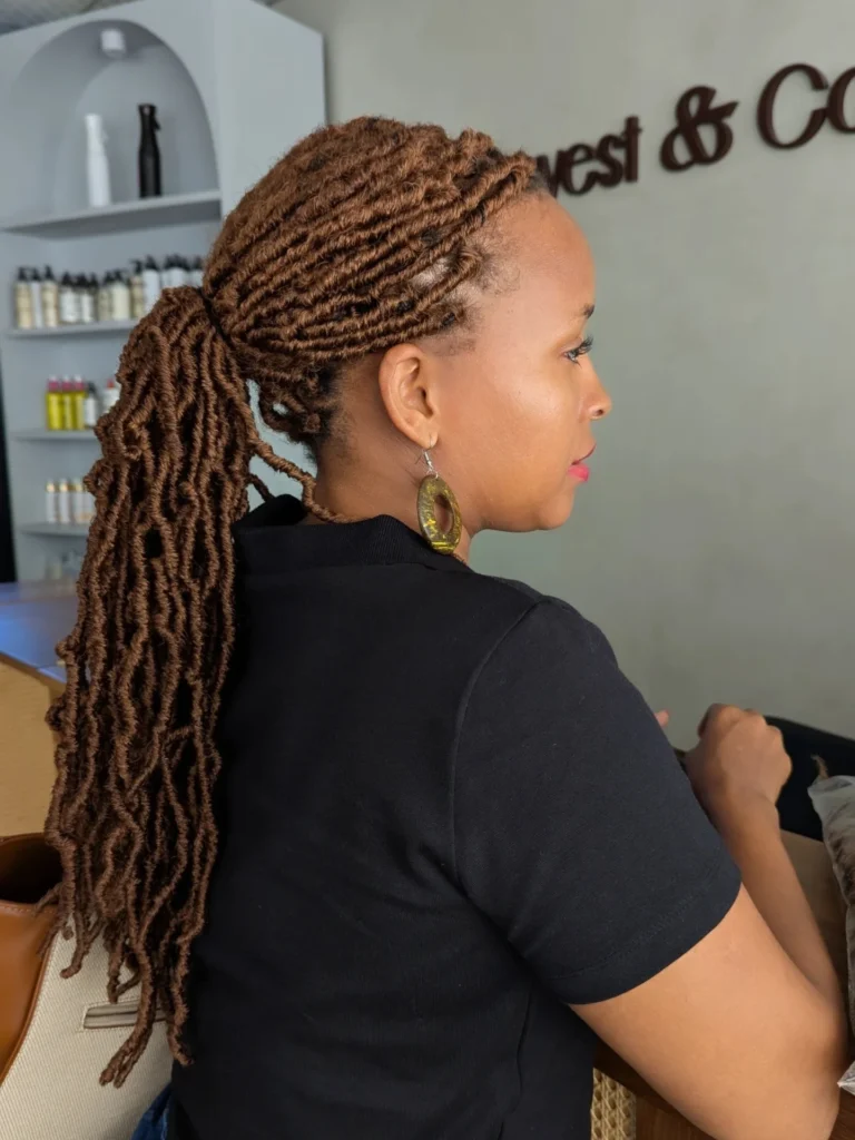 A woman with faux locs styled into a low ponytail with a neat and polished finish.