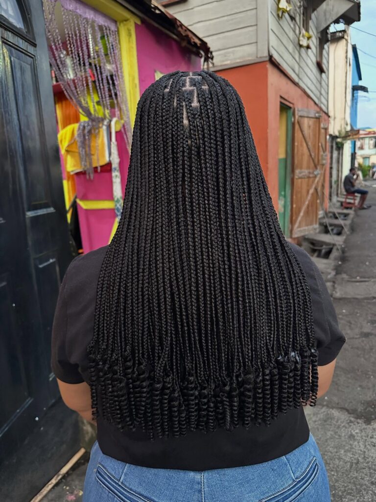 A woman with long small box braids featuring neat parts and softly curled ends.