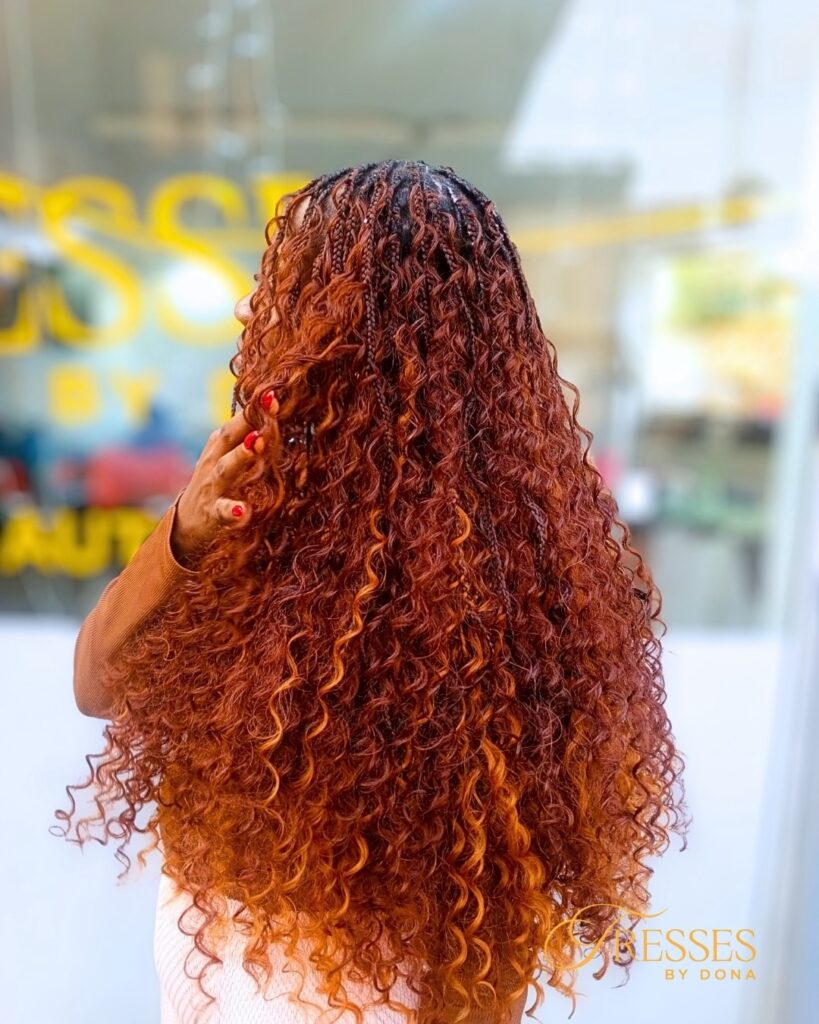 A woman with long defined curly hair featuring warm copper highlights and layered texture.