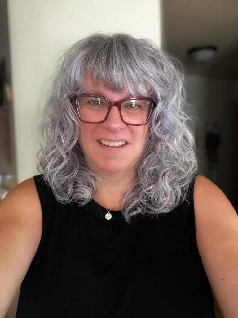 Shoulder length curly gray bob with soft bangs and loose natural curls.