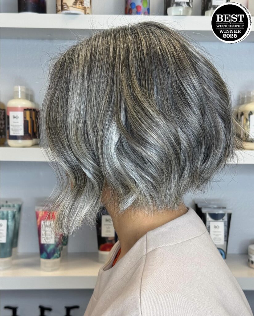 Chin length curly gray bob with soft waves and blended silver tones viewed from the side.