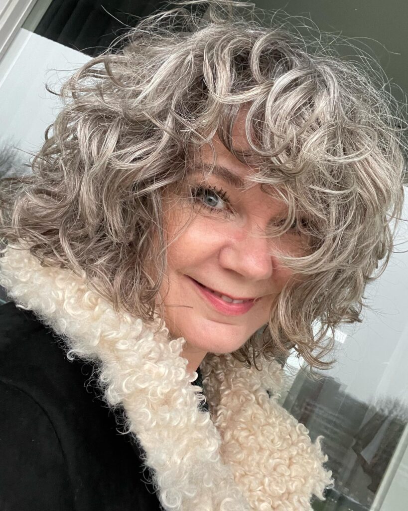 Tousled curly gray bob with defined curls and natural volume styled in a casual look.