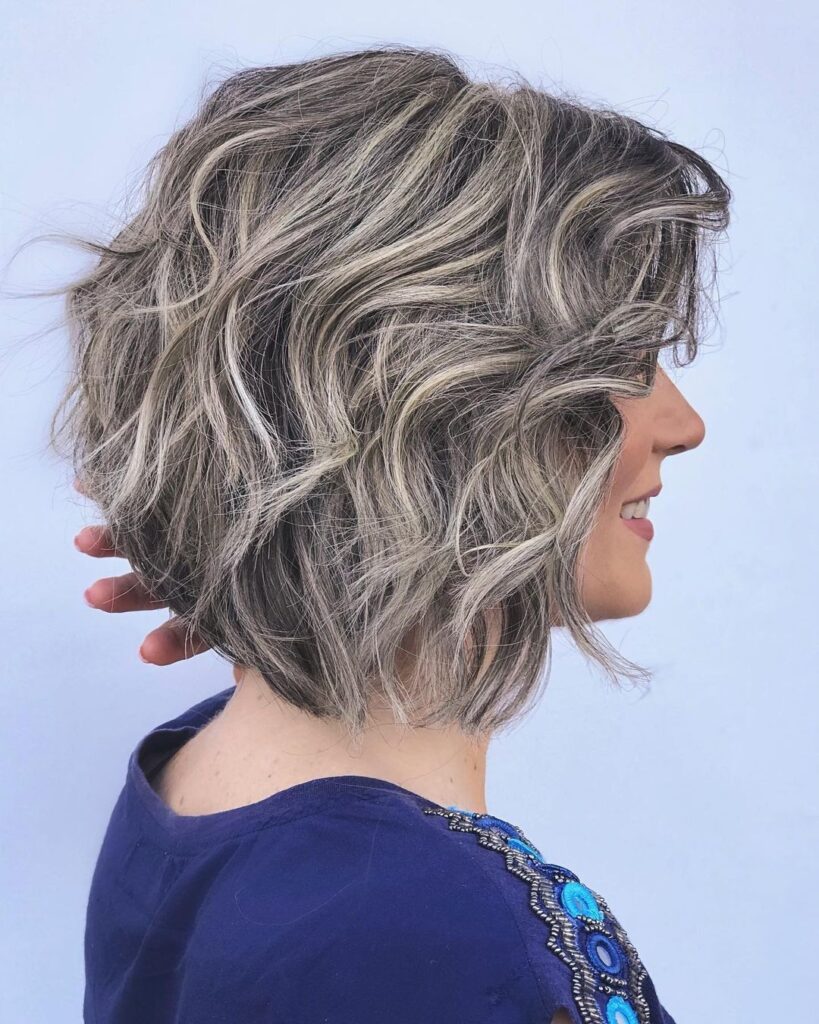 Layered curly gray bob with voluminous waves and soft highlights styled with natural movement.