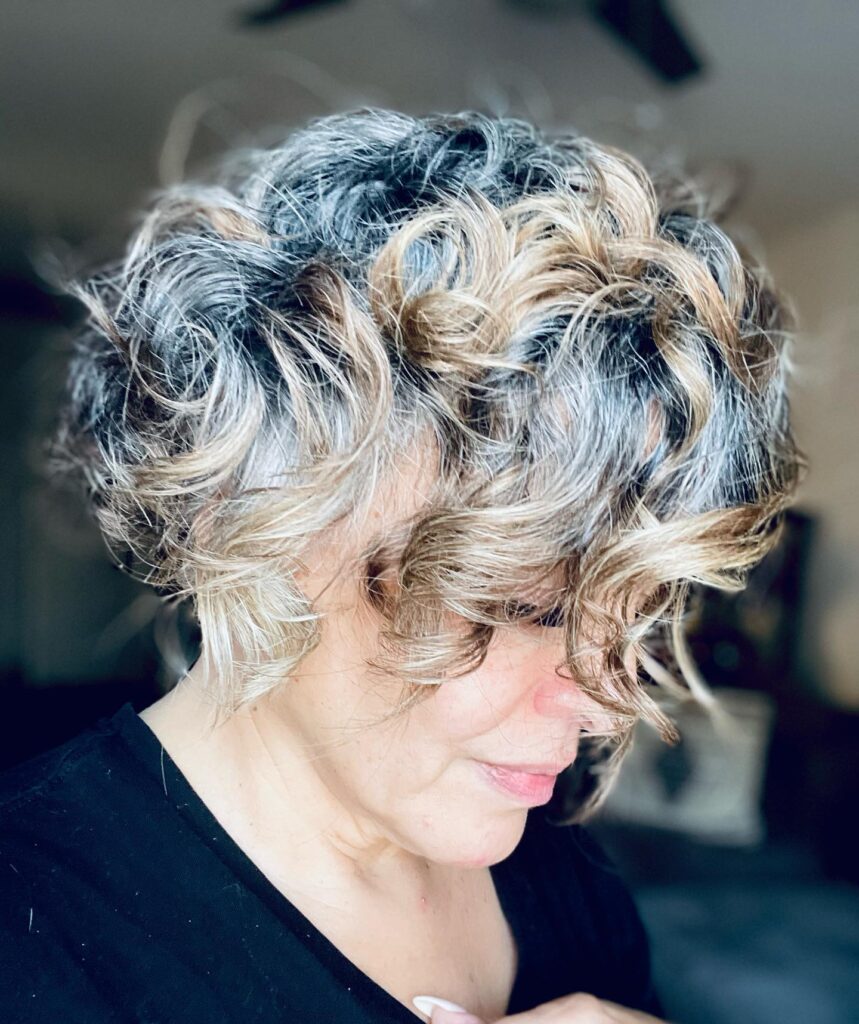 Curly gray bob with tousled texture and blended warm highlights throughout.