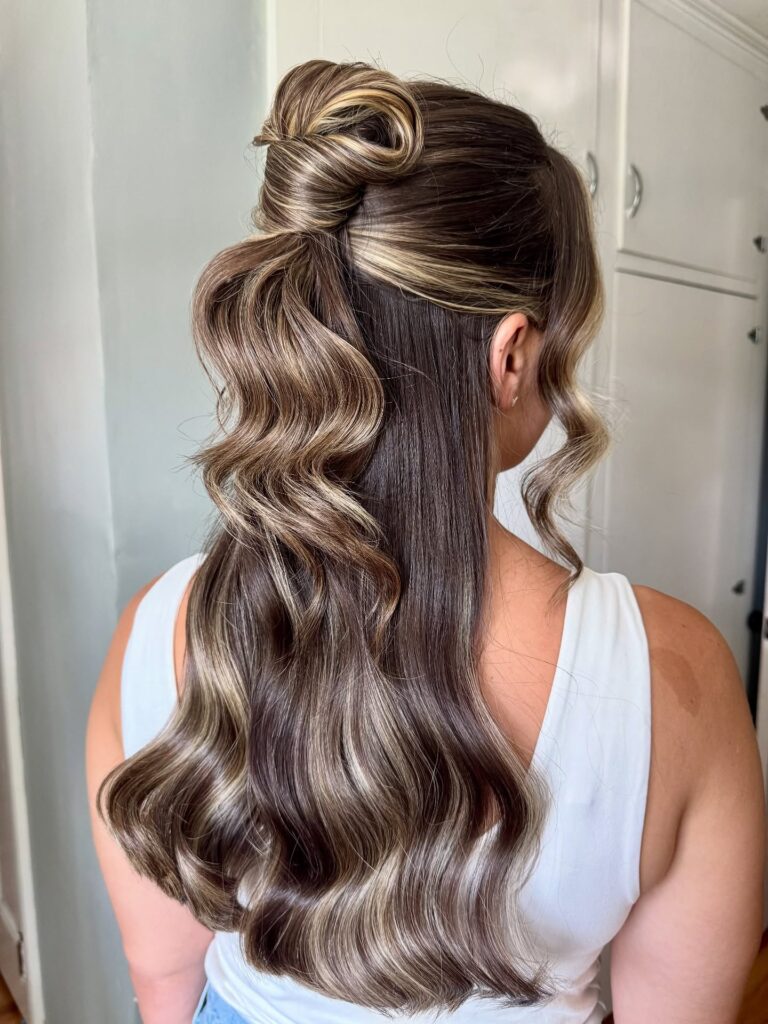 Long highlighted brunette hair styled in a sleek half up knot with soft glossy waves.