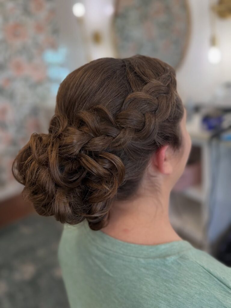 Long brunette curly hair styled into a braided low bun with soft textured detail.