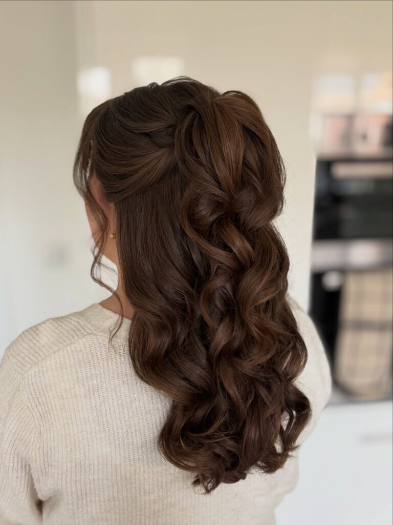 Long brunette curly hair styled in a soft half up twist with loose flowing waves down the back.