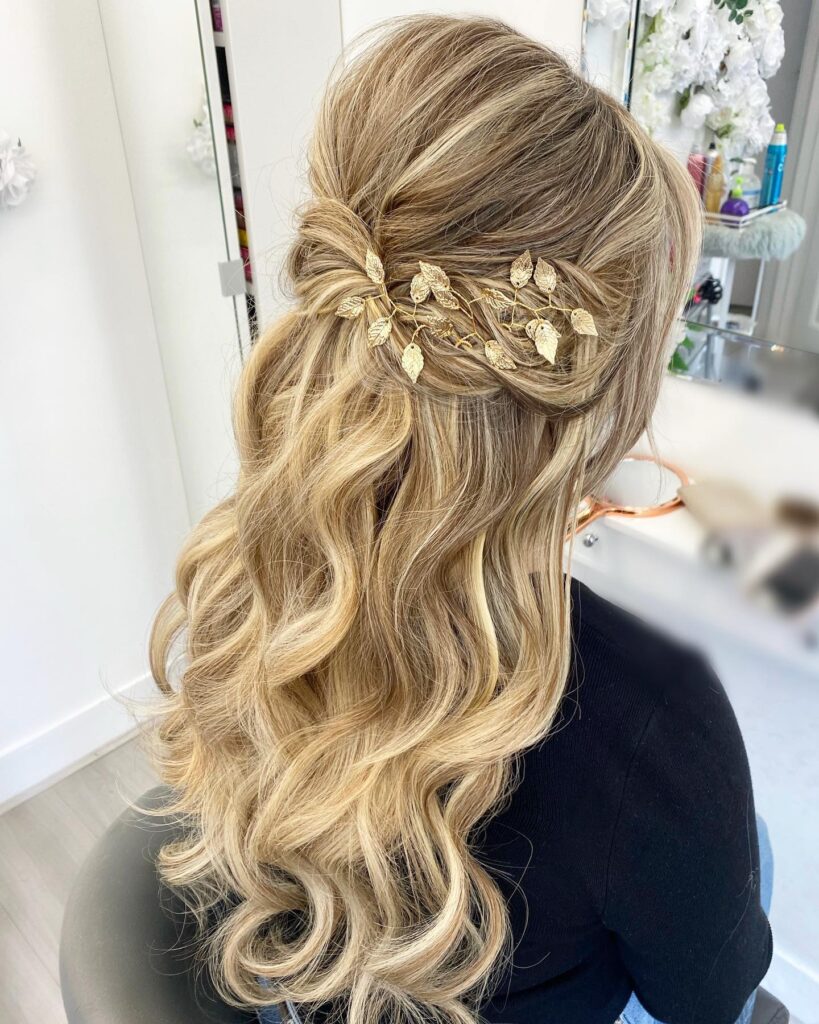Long blonde curly hair styled half up with a gold leaf hair accessory and soft waves.