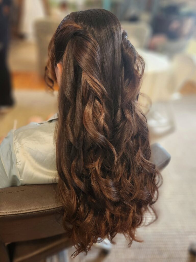 Long layered curly brown hair styled in a loose half up hairstyle with soft natural waves.