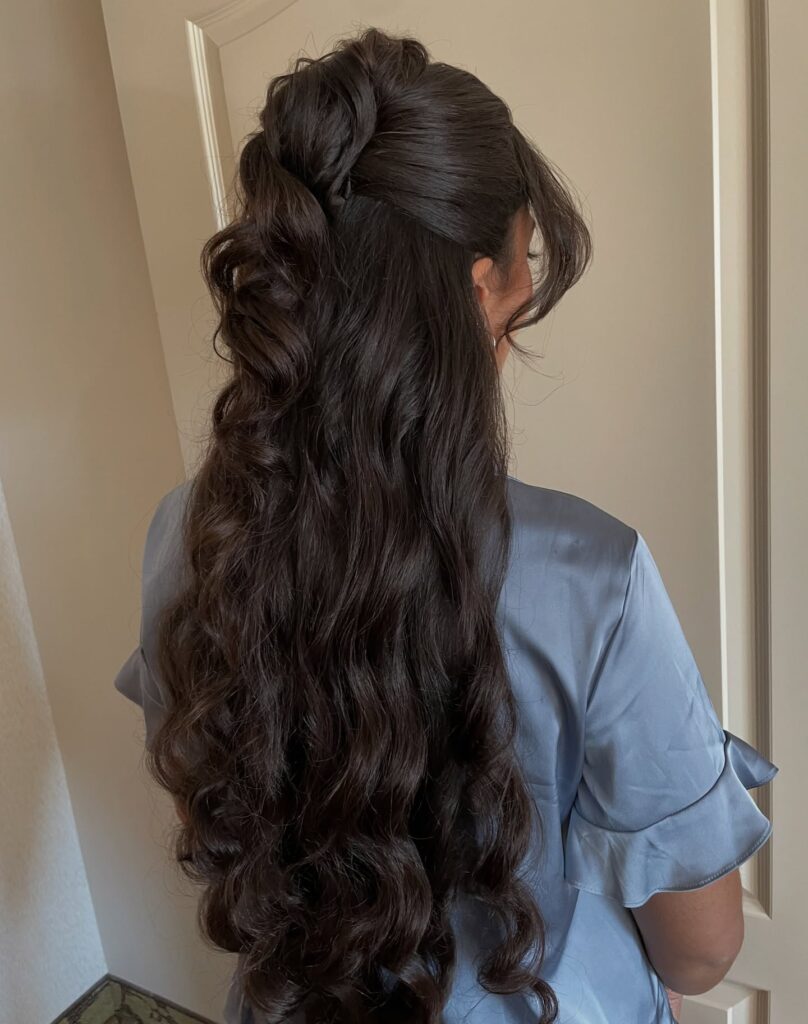 Long dark curly hair styled half up with volume and textured curls flowing down.