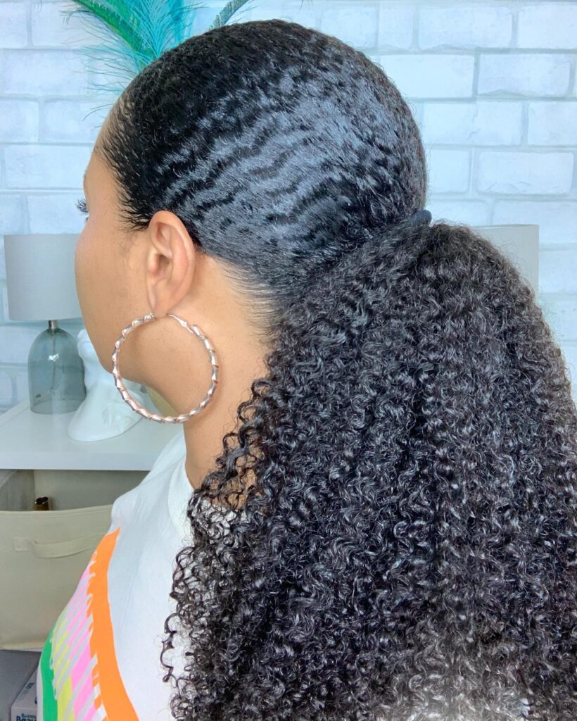 Sleek low ponytail with wave patterns at the roots and a full curly natural hair tail.