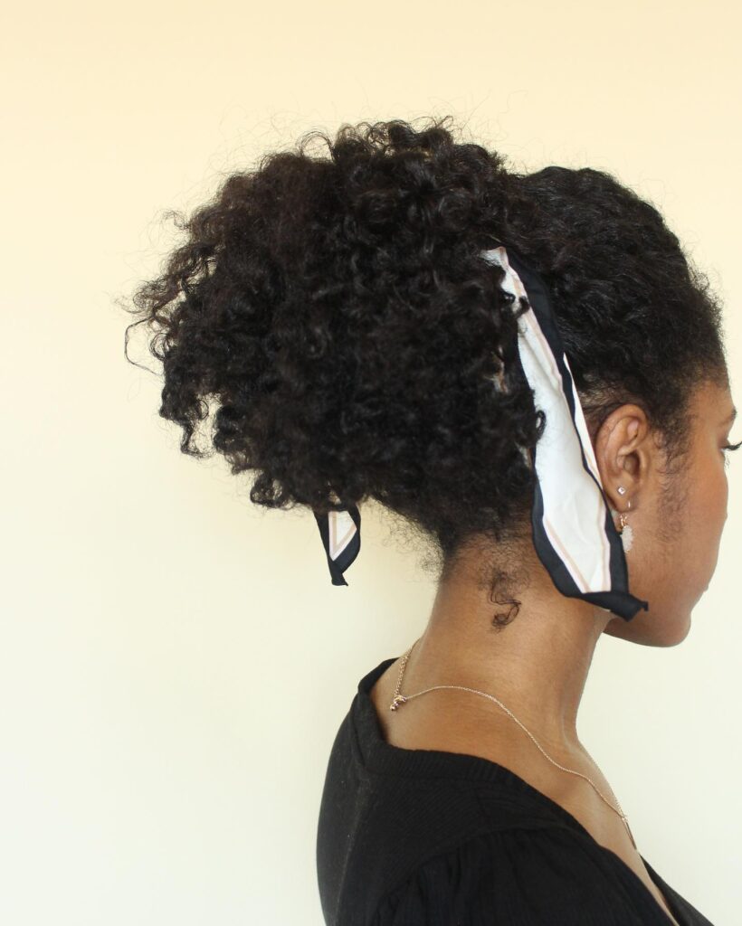 Sleek ponytail with a voluminous curly puff tied with a scarf.