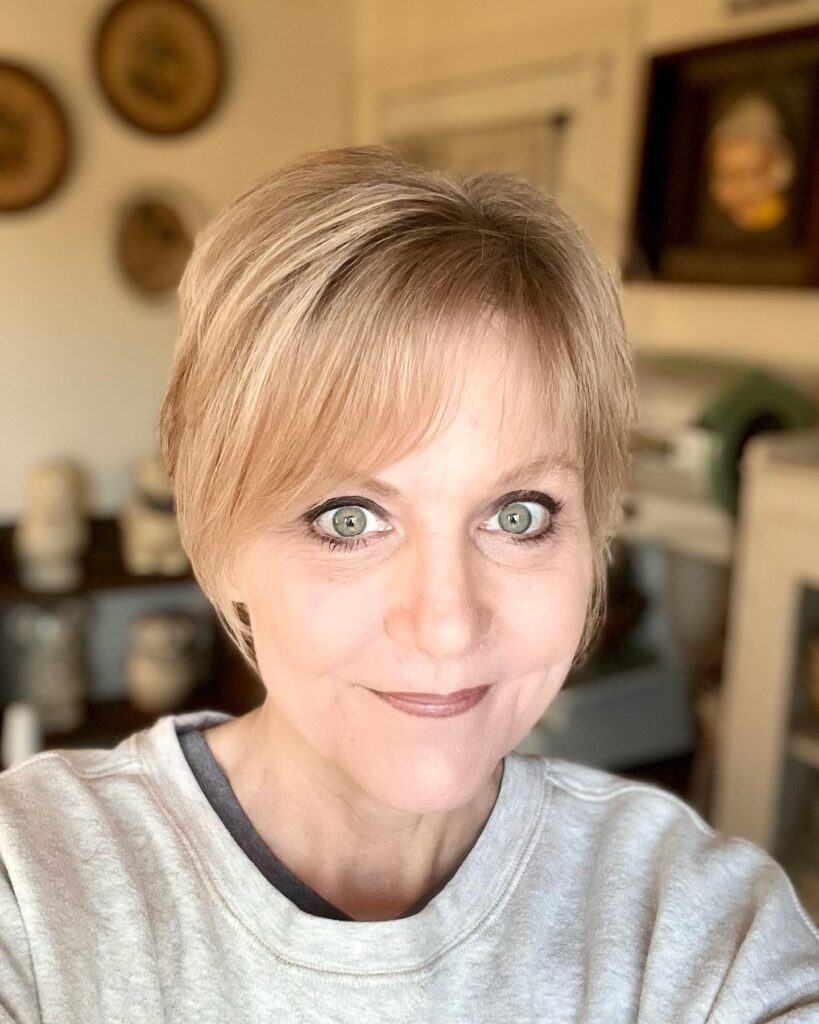 A woman with a short pixie haircut and soft wispy bangs in a warm blonde tone.