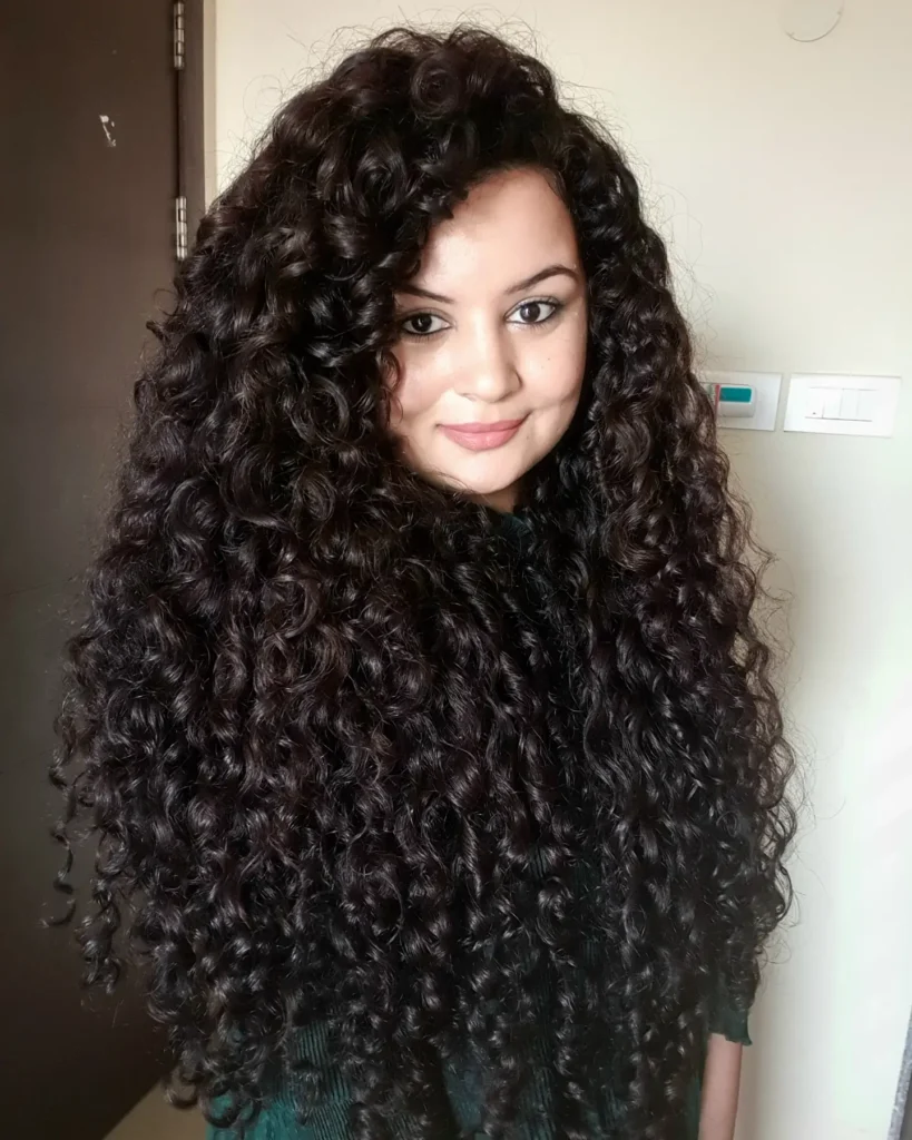 Long dark hair with tight spiral curls styled for maximum volume and fullness.