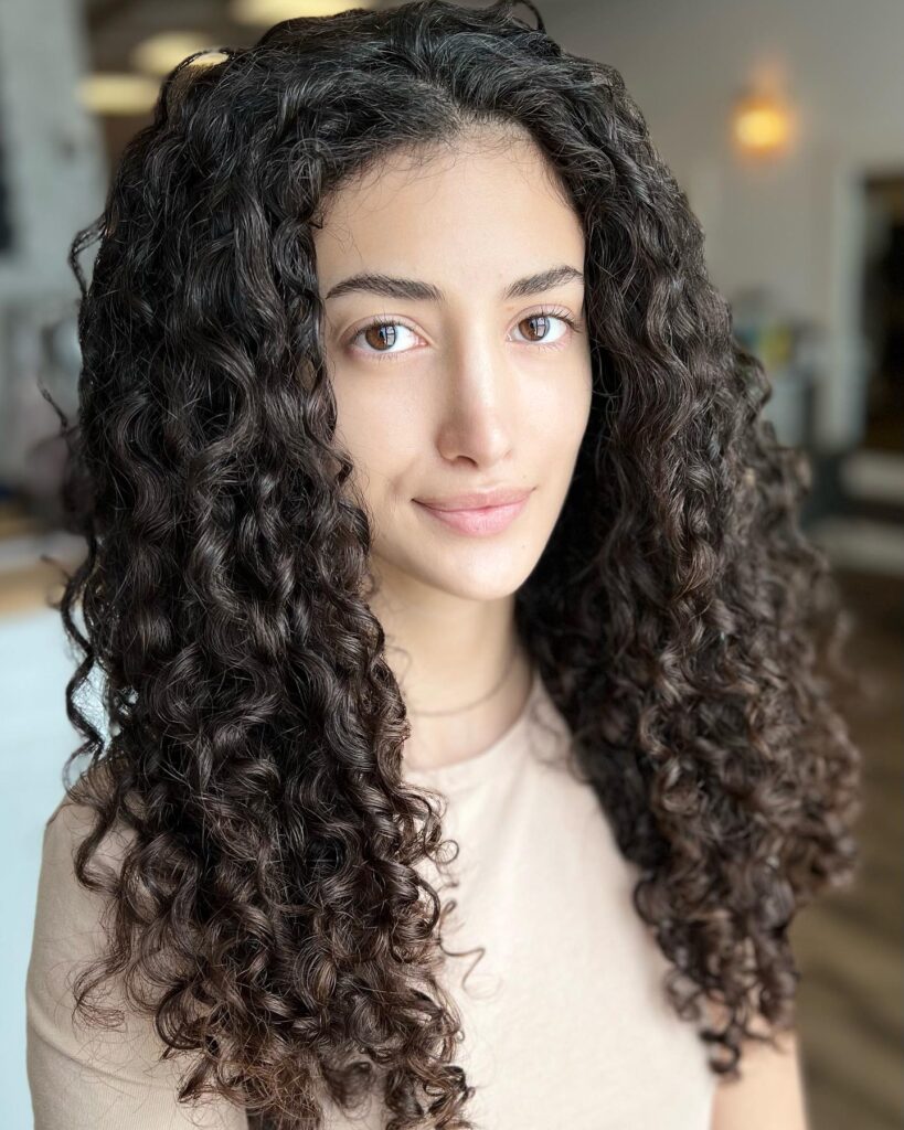 Long layered curly hair with soft natural texture and light volume around the face.