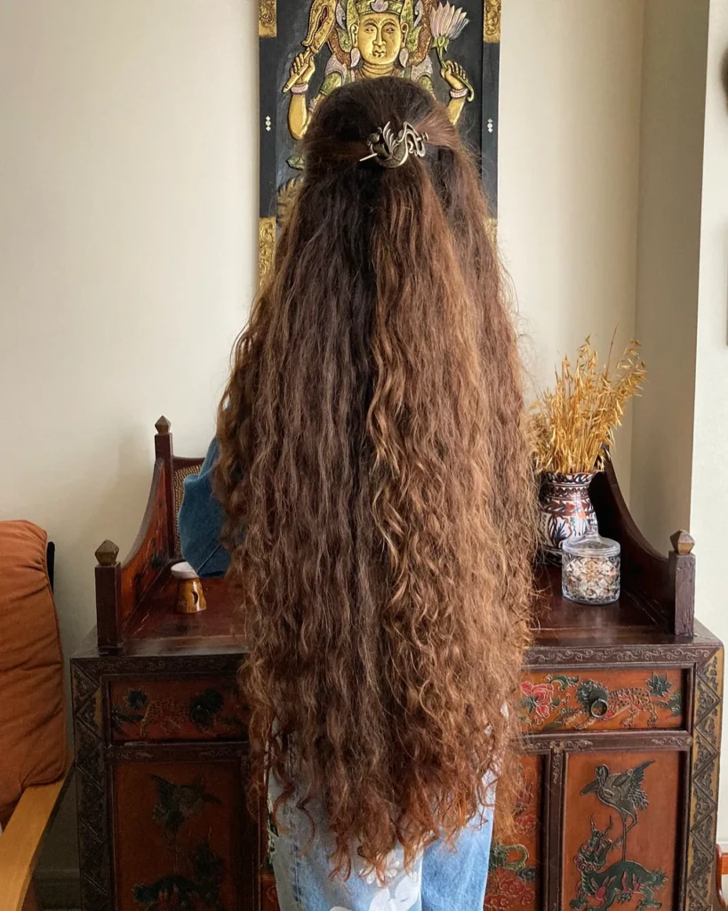 Long soft curly hair styled half up with a clip and natural loose texture.