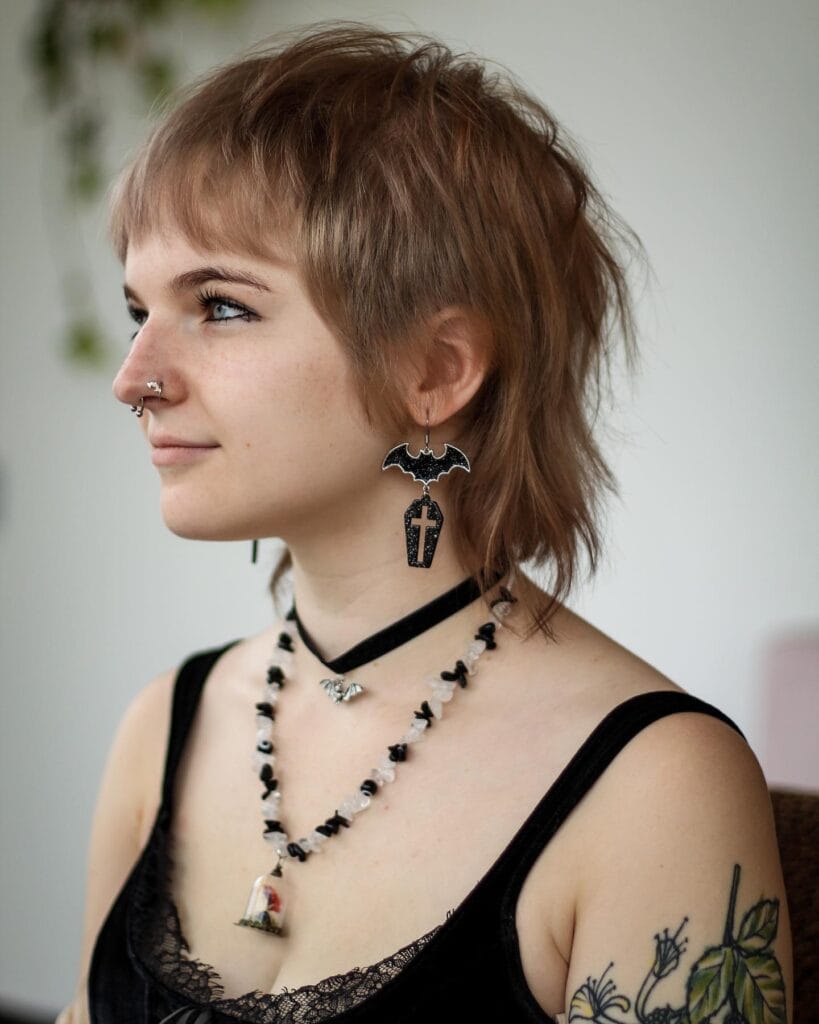 A woman with a short mullet style tomboy haircut featuring soft layers, baby bangs, and a natural light brown color.