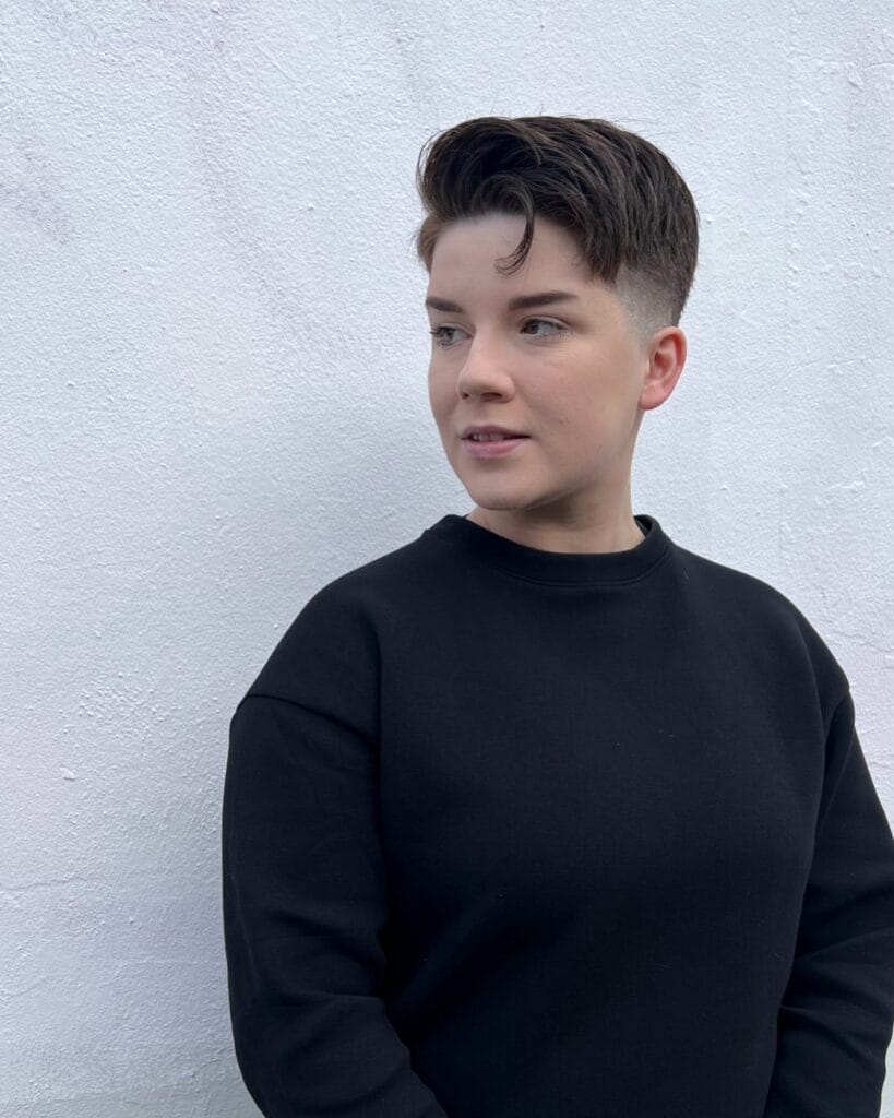 A woman with a short tomboy haircut featuring faded sides and a textured longer top styled with natural volume.