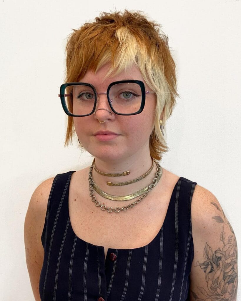 A woman with a short shaggy tomboy haircut featuring choppy layers and a two tone blend of copper and blonde hair.