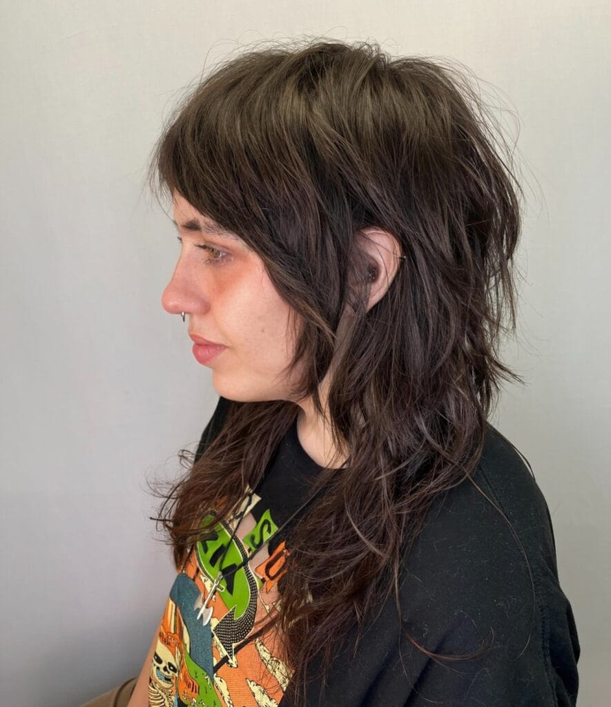 A woman with a layered wolf cut hairstyle featuring medium length dark brown hair with soft choppy layers and light fringe.