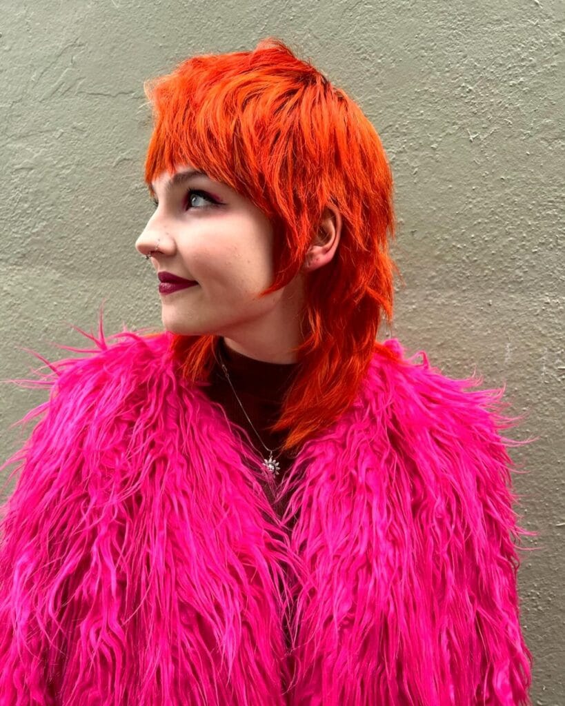 A woman with a bright red tomboy mullet haircut featuring choppy layers, short fringe, and a longer textured back.