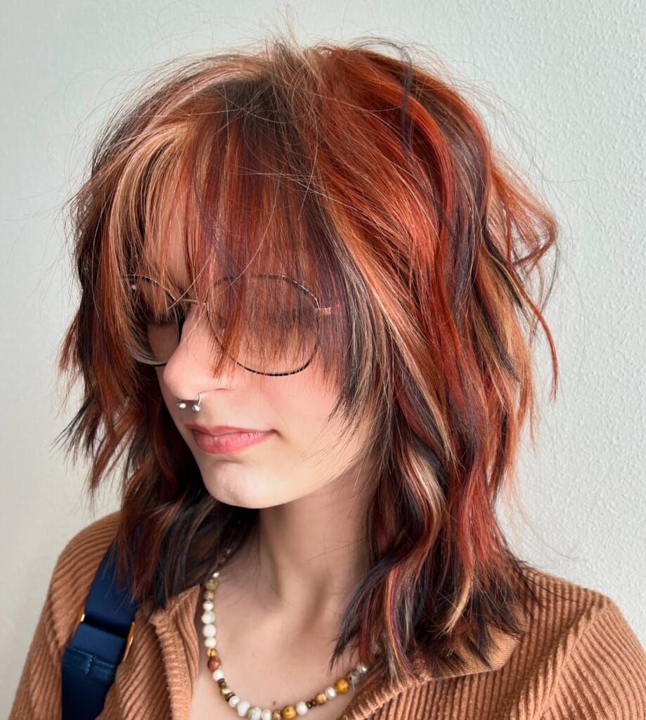 A woman with a shaggy layered bob featuring choppy ends and copper and auburn highlights with a soft fringe.