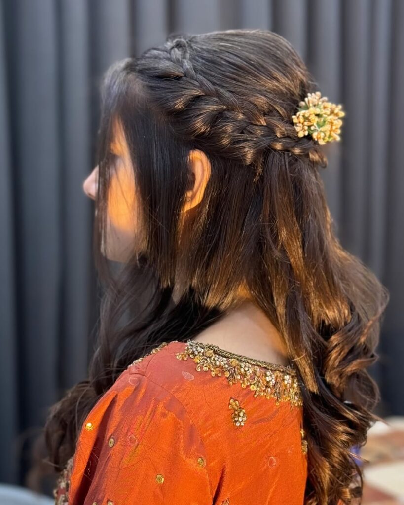 Half up side braid with long soft wavy hair and a small floral accessory.