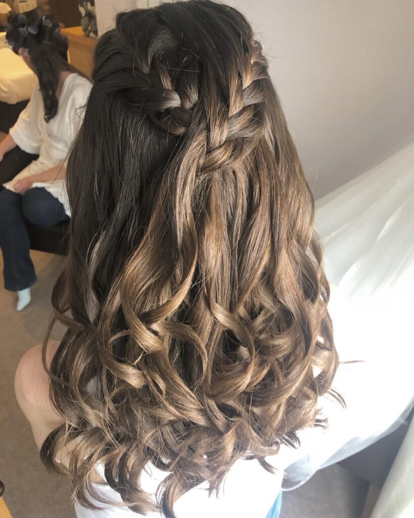 Waterfall braid woven into long soft brunette curls with natural highlights.