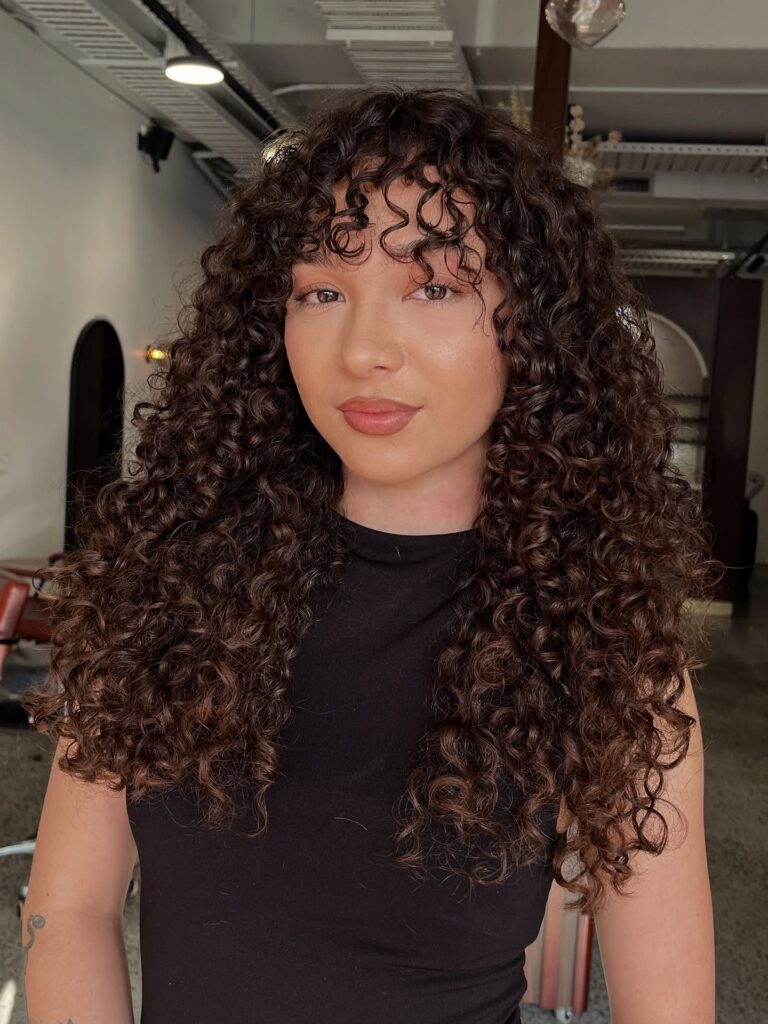 Long defined glossy curls with soft separated curly bangs framing the face.
