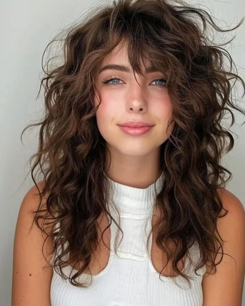 Loose tousled curly layers with soft side swept bangs and natural texture.