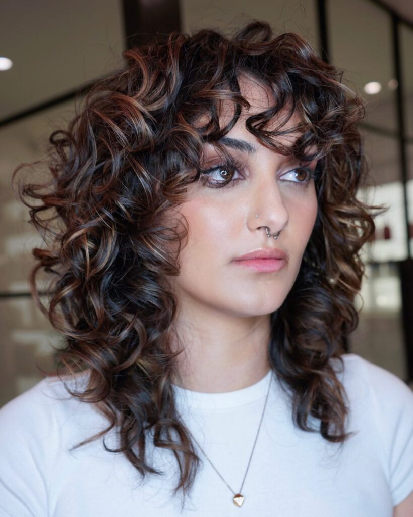 Voluminous curly shag haircut with layered curls and a textured curly fringe.