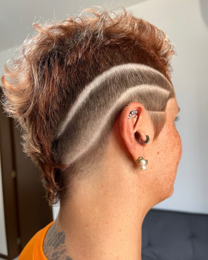 A short tomboy haircut with a shaved undercut design featuring curved lines and a textured copper top.