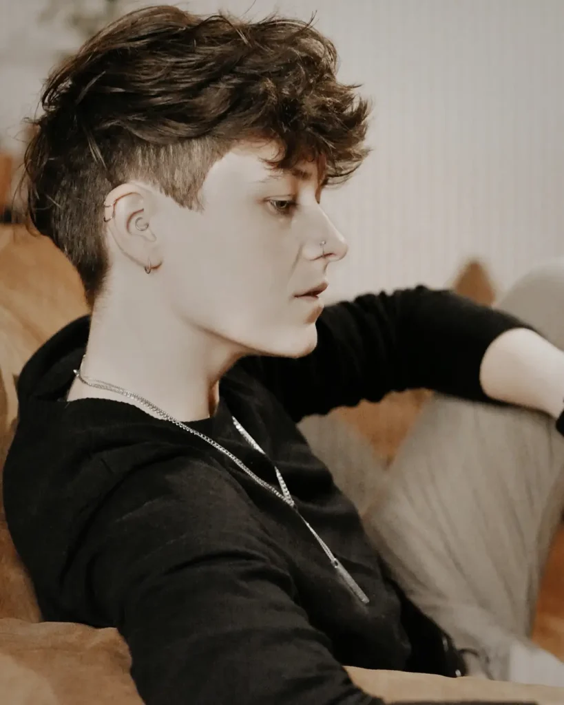 A tomboy haircut with shaved sides and a longer curly textured top in a dark brown shade.
